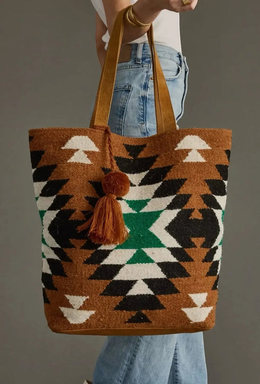 Sighthound Designs woven tote bag with Southwestern geometric pattern in brown, black, white, and green. Faux leather straps and tassel detail.